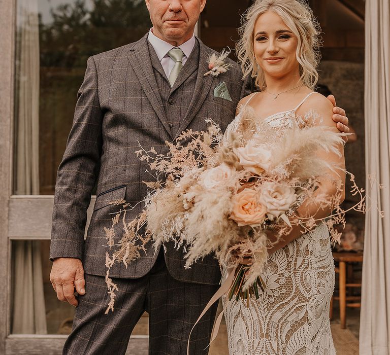 Father of the bride in grey checkered three piece suit with a sage green tie and pocket square with the bride in a boho gown smiling together