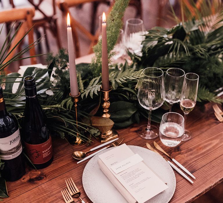 Neutral wedding candles in gold holders with neutral speckled plating with menu and napkin and white and gold cutlery for greenery them wedding 