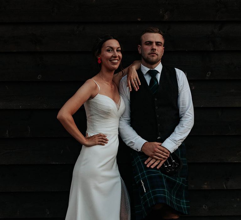 Stylish bride and groom in a Stephanie Allin bridal gown with polka dot tule overlay, front slit and trainers and a tartan kilt