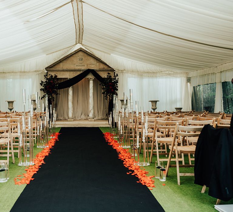 Parley Manor marquee wedding with black aisle carpet with red rose bushes and red rose petals, crystal candle decor, and black wedding drapes 