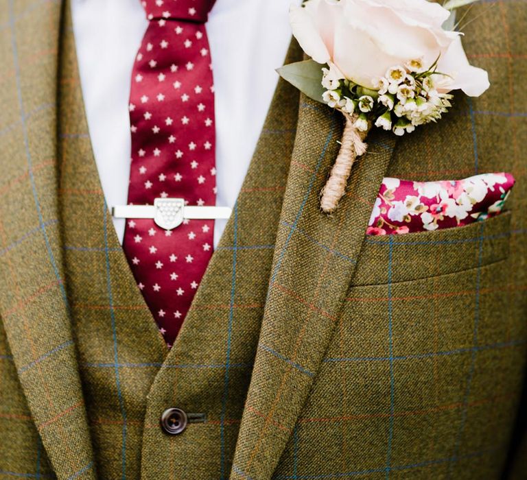 Olive coloured three piece groom suit with red and blue checkered lines with a burgundy star tie and burgundy floral pocket square 