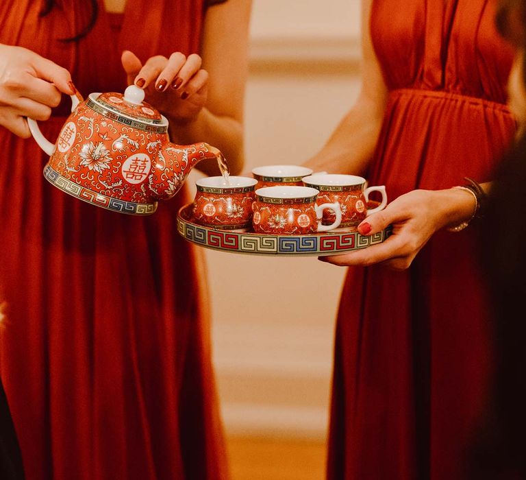 Bridesmaids in red halterneck bridesmaid dresses pouring tea from Chinese teapot into small tea cups at Chinese Tea Ceremony wedding