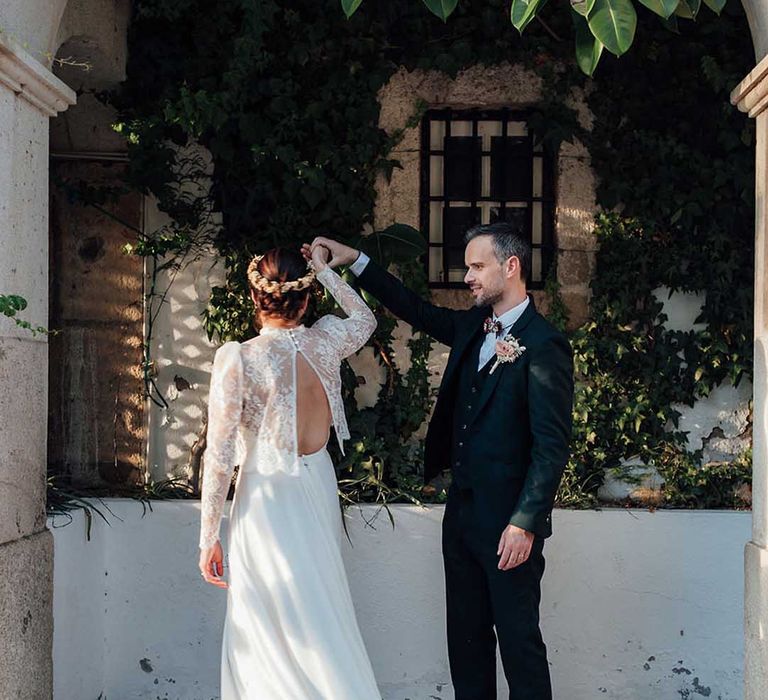 groom in black suit twirling his bride in slip wedding dress with lace jacket 