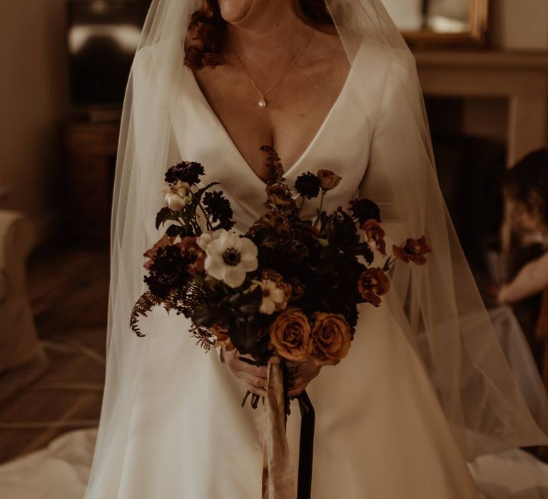 Bride in long sleeve deep v wedding dress and church length veil holding white, dusky pink and burnt red dried flower, rose and peony bridal bouquet 