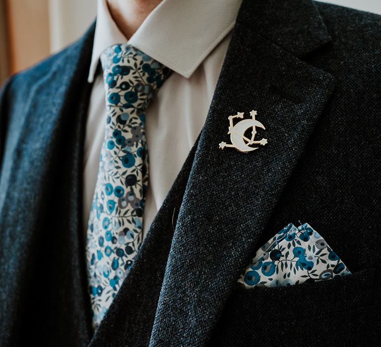 Groom in a three piece blue suit with a blue and white floral tie and pocket square with a moon and stars pin accessory 