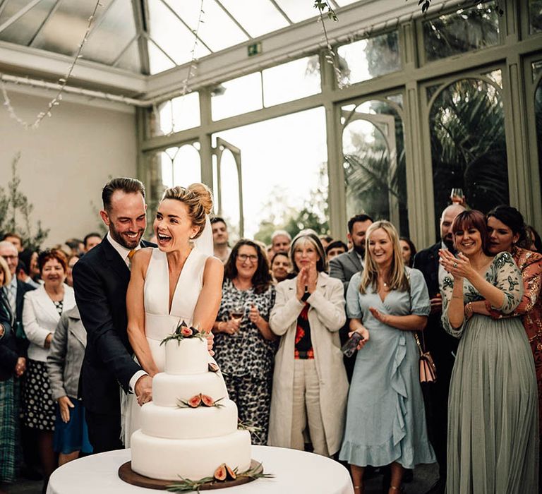 The bride and groom cut their classic white wedding cake with four tiers and figs 