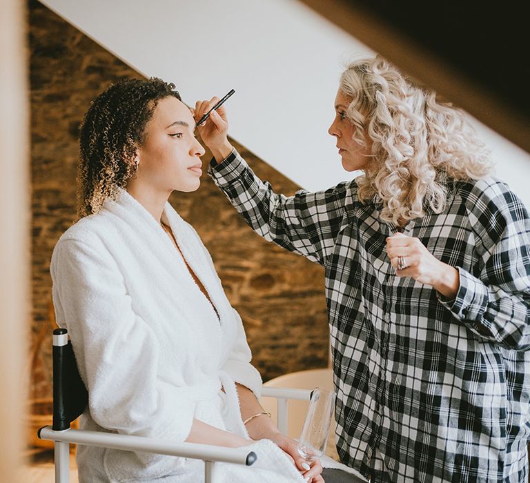 Bride sitting in white robe getting her makeup done for the wedding 