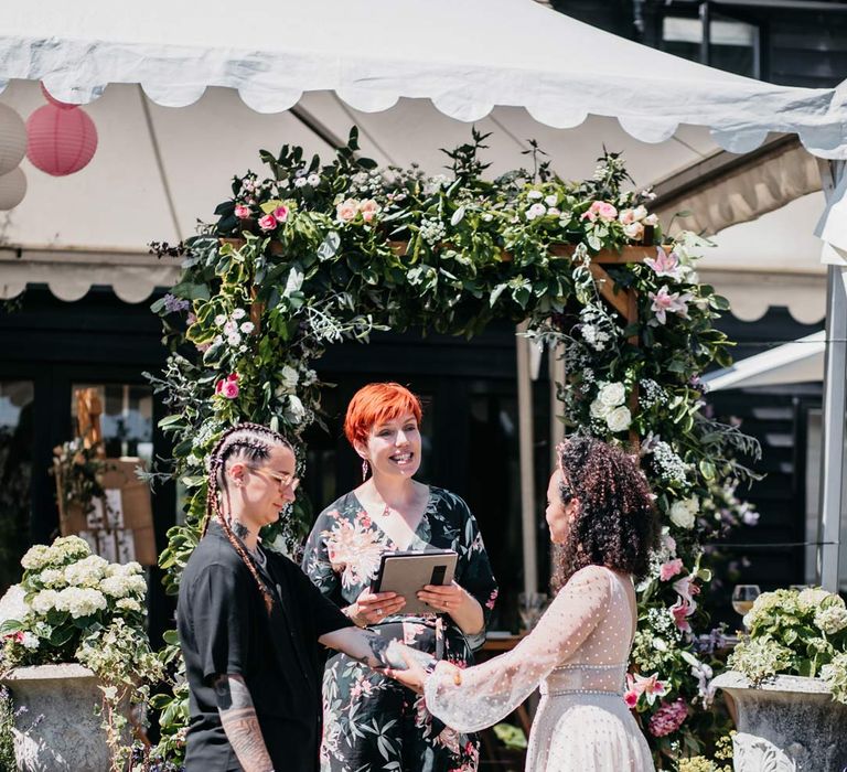 Bride in long sleeve v-neck sheer polka dot overlay sparkly wedding dress and gold celestial bridal headband doing handfasting ceremony with bride in black shirt and black trousers at Viking themed wedding at Viking inspired wedding