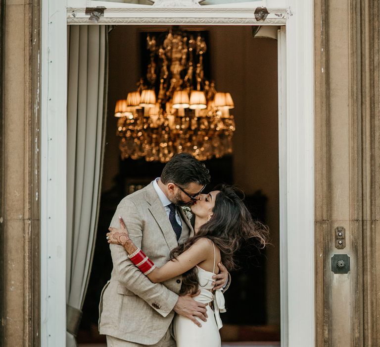 Groom in three piece light wedding suit posing with the bride for their couple portrait at their elegant multicultural wedding 