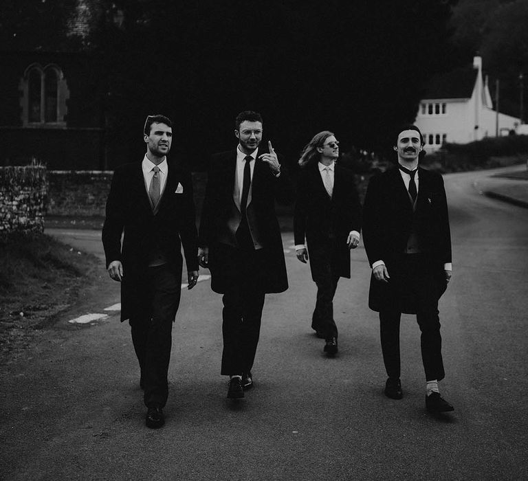 The groomsmen walk together like a boy band in morning suits 