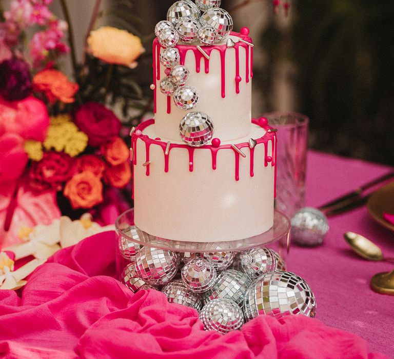 Two tier white iced wedding cake with pink drip icing, mini disco balls and metallic sprinkles 