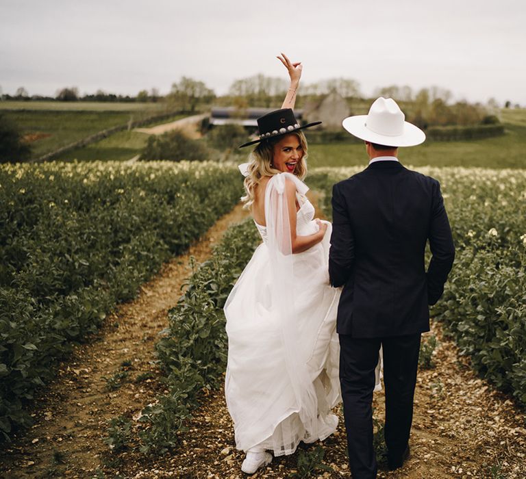 Bride in princess wedding dress by Eva Lendel with bow wings and groom in black tuxedo wearing black and white cowboy hats 