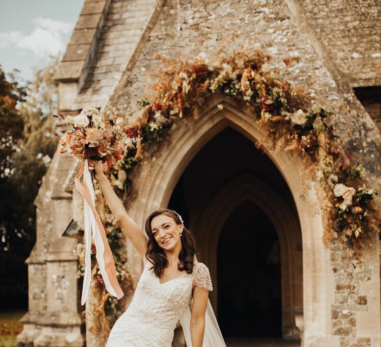 Bride in beaded lace style wedding dress with autumnal bouquet 