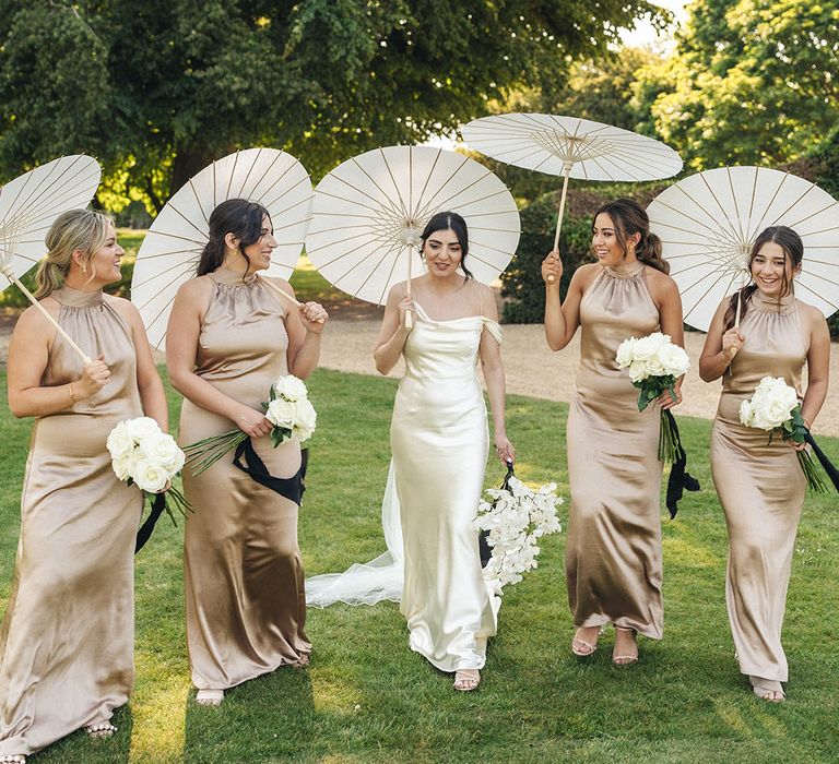 Bridesmaids wearing gold bridesmaid dresses with umbrellas at hot summer wedding 