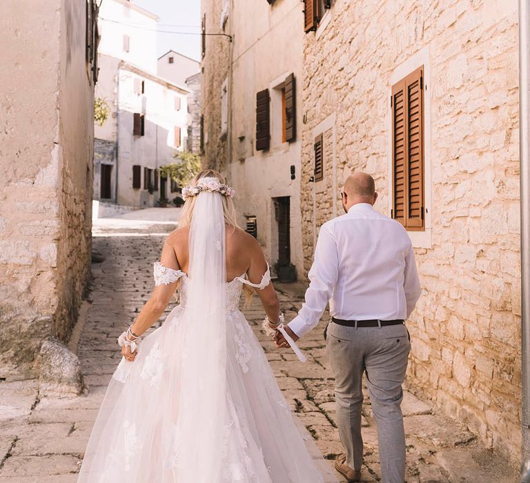 Bride in floral lace wedding dress walking around the streets of Croatia with the groom 