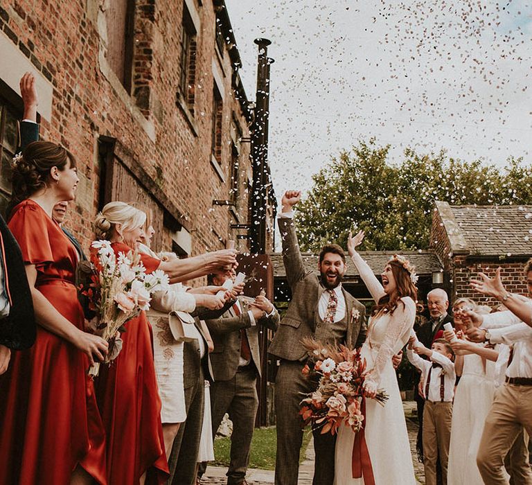 Confetti exit for bride and groom at industrial wedding with autumnal theme and dark brown and orange wedding outfits 