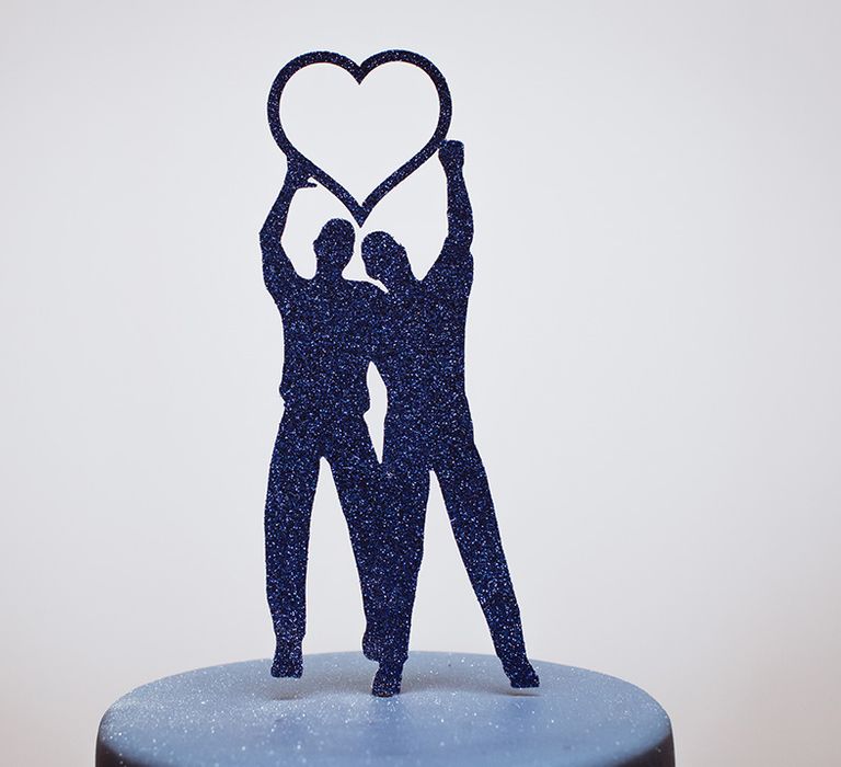 Blue glitter wedding cake topper of two men holding a giant heart 