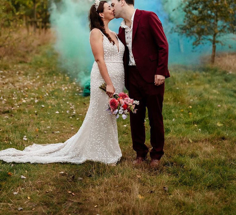 Bride and groom kiss surrounded by blue and green colourful smoke flares 