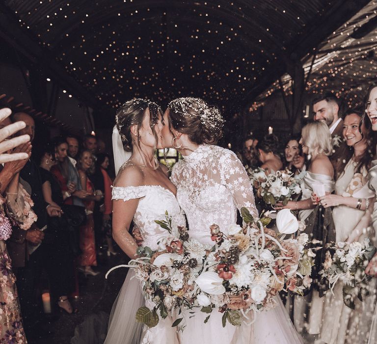 Brides share a kiss at their rustic Stone Barn wedding with dried confetti 