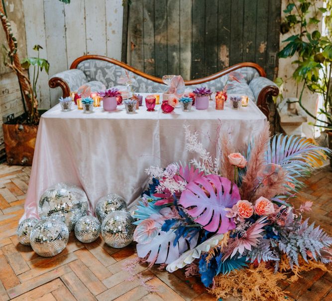 Colourful sweetheart table with iridescent flowers, disco balls and votives. 