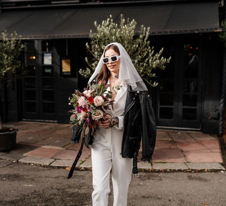 Stylish bride in jumpsuit, polka dot veil and leather jacket 