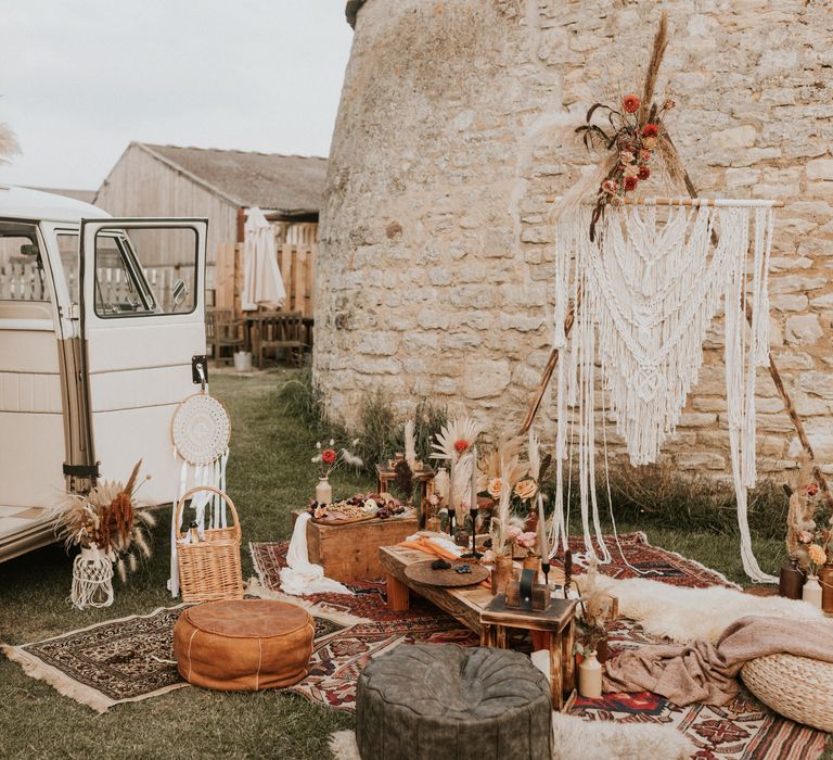 Camper van next to Macrame backdrop with wooden tables and trunks with grazing plates