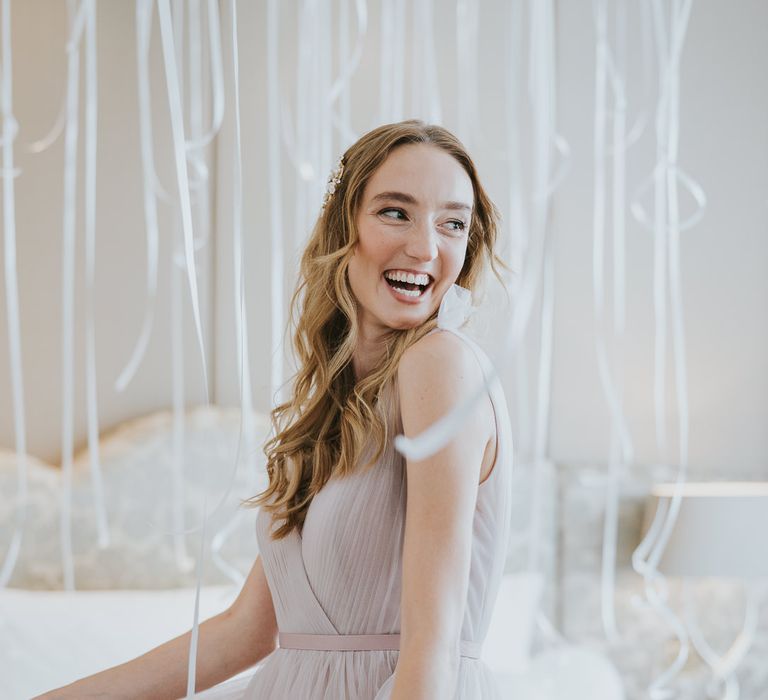 Bridesmaid with blonde wavy hair wearing a blush pink chiffon dress from TH&TH Bridesmaids