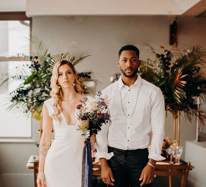 Intimate wedding with groom in leather trousers and white skirt and bride in a fitted wedding dress holding a moody dark wedding flowers bouquet 