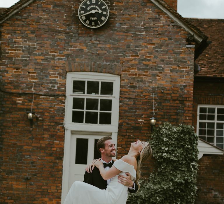 Groom picks up bride outside barn as they laugh together