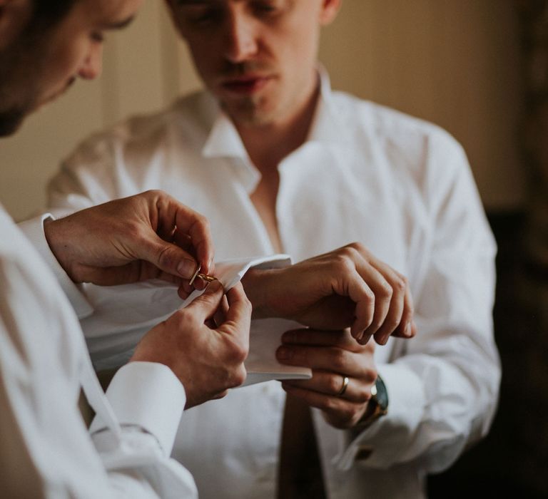 Groomsmen in white shirts putting on cufflinks at Caswell House wedding