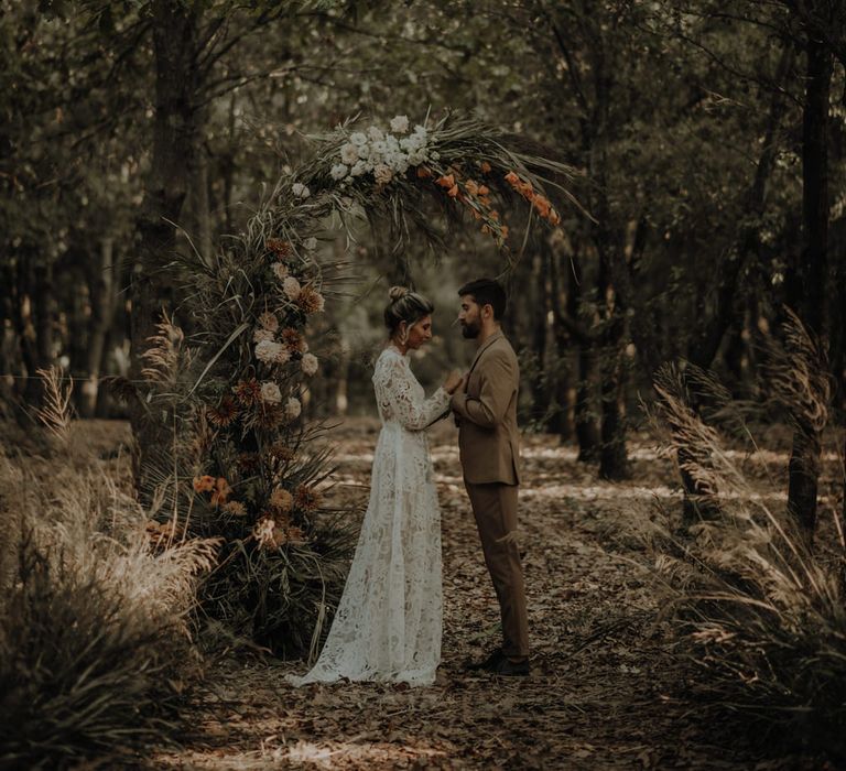 Bride and groom standing at a fresh and dried flower arch in the middle of a forest 