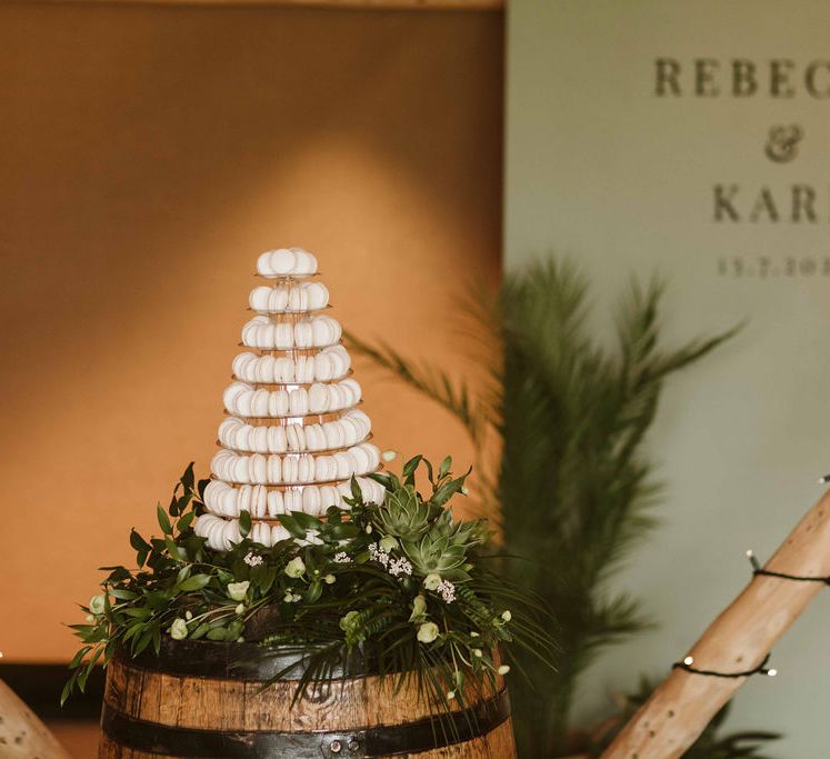 White macaroon tower stands upon wooden barrel with green personalised stationery in the background