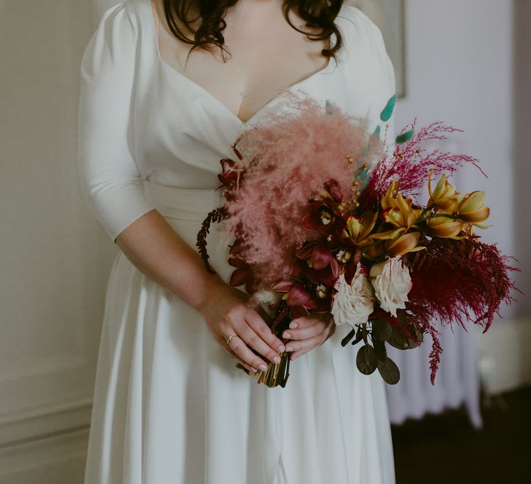 Bride in white cat eye glasses, bridal headband and Rime Arodaky wedding dress holds white and pink rose and pampas grass wedding bouquet