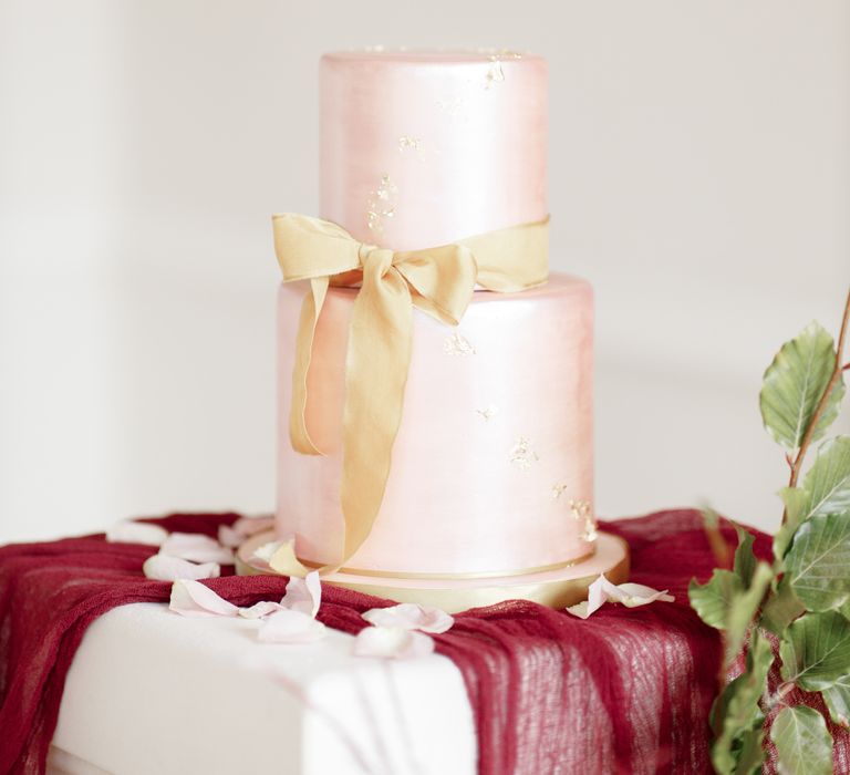 Pale pink wedding cake tied with gold ribbon