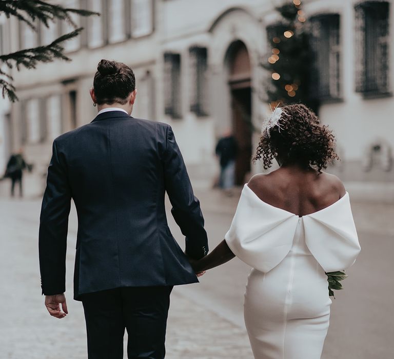 Bride & groom walk together hand in hand outdoors