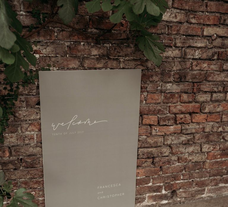 Contemporary wedding welcome sign propped up against and exposed brick wall