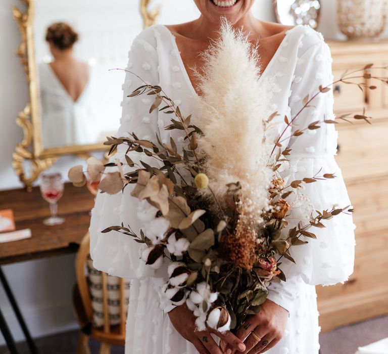 Bride smiling in boho wedding dress holding pampas grass and dried foliage bouquet