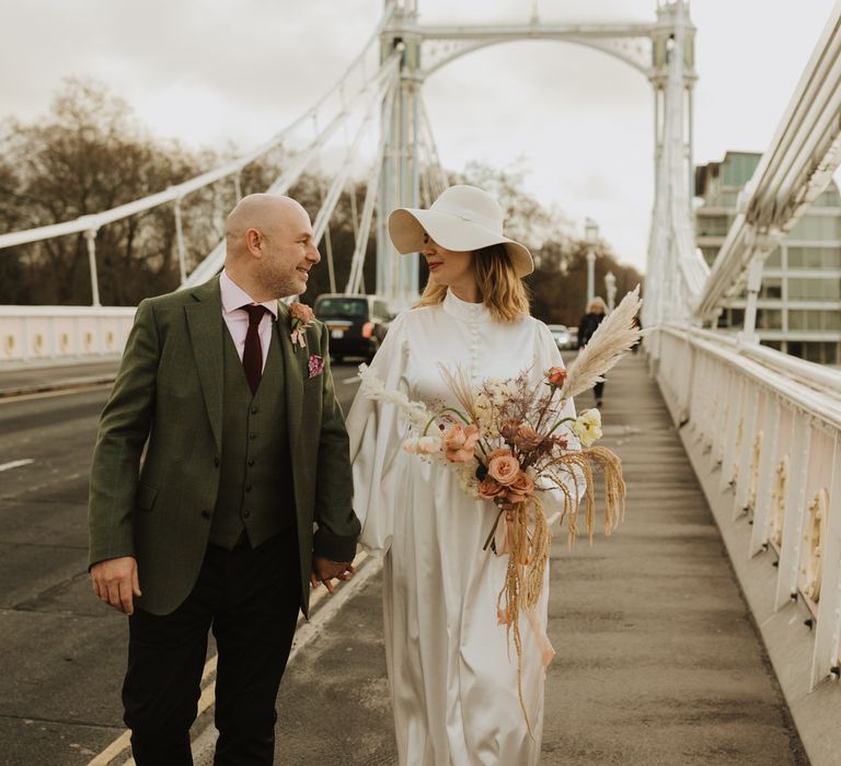 Bride & groom walk across bride in London whilst holding hands and smiling