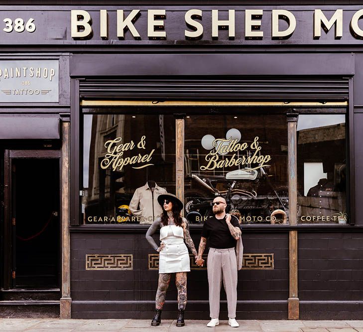 Alternative bride and groom standing outside a tattoo parlour at micro wedding 