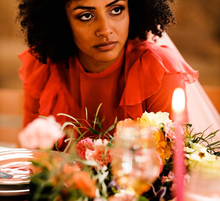 Black bride in a red wedding dress with afro hair sitting at the wedding breakfast table 