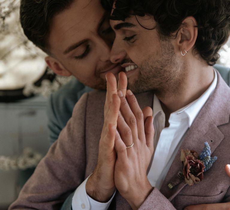 Grooms sit together whilst clasping hands together on wedding day