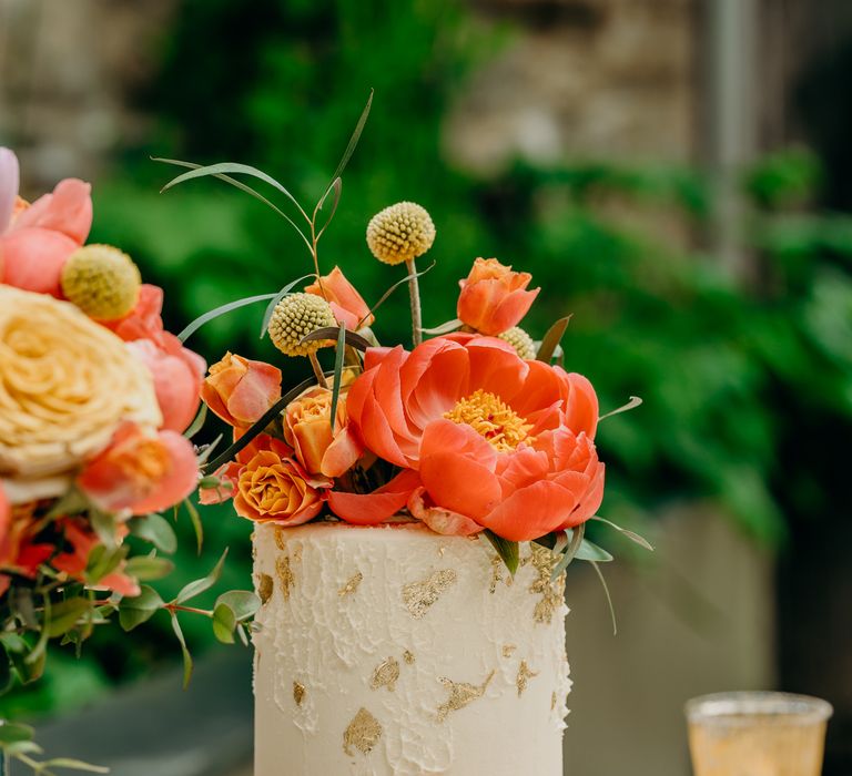 Wedding cake with white frosting, gold leaf detailing and bright floral decor