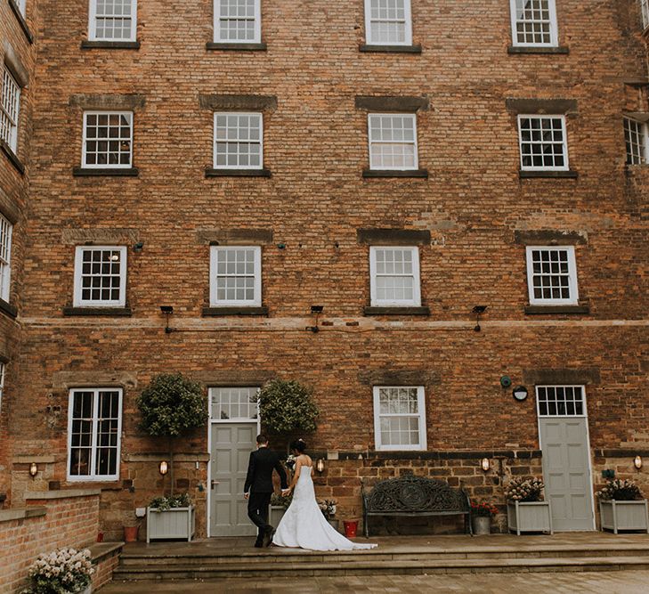 A bride in sophia Tolli walks into her wedding venue with her husband.