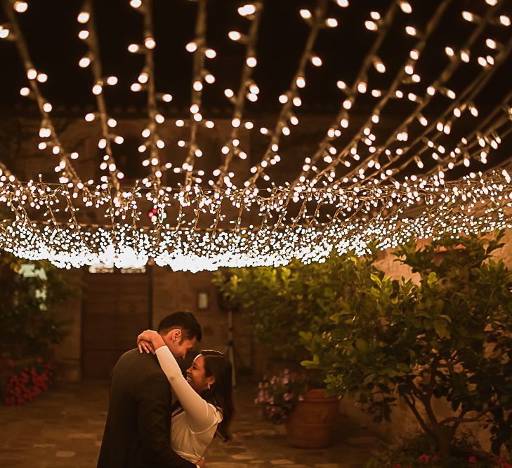 Twinkling fairy lights above dancing couple sparkle in the night for outdoor wedding reception