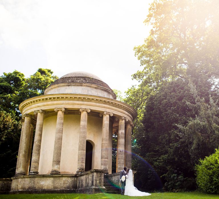 Light shines through the trees as bride & groom walk through grounds on their wedding day