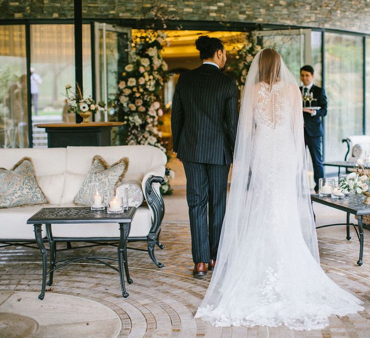 Classic bride in a lace Pronovias wedding dress and cathedral length veil entering the elegant wedding reception at Grantley Hall wedding venue in Yorkshire with her groom 