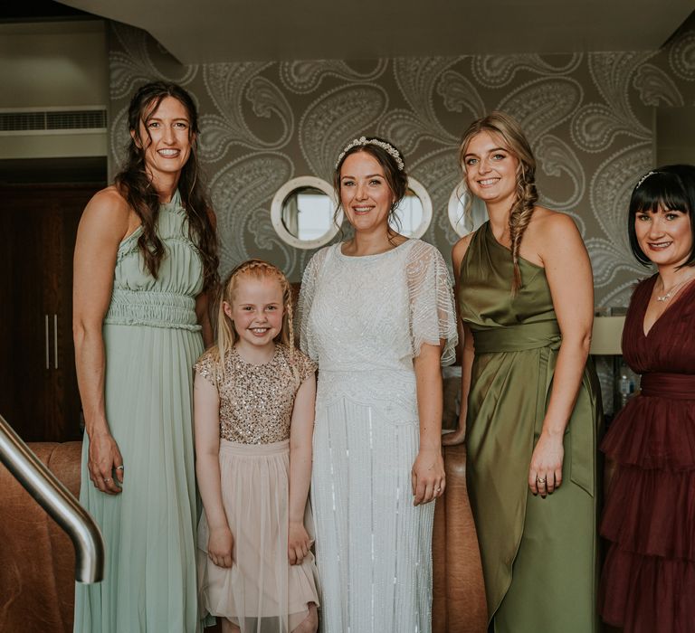 Bride stands with her bridal party who wear different coloured and styled bridesmaids dresses