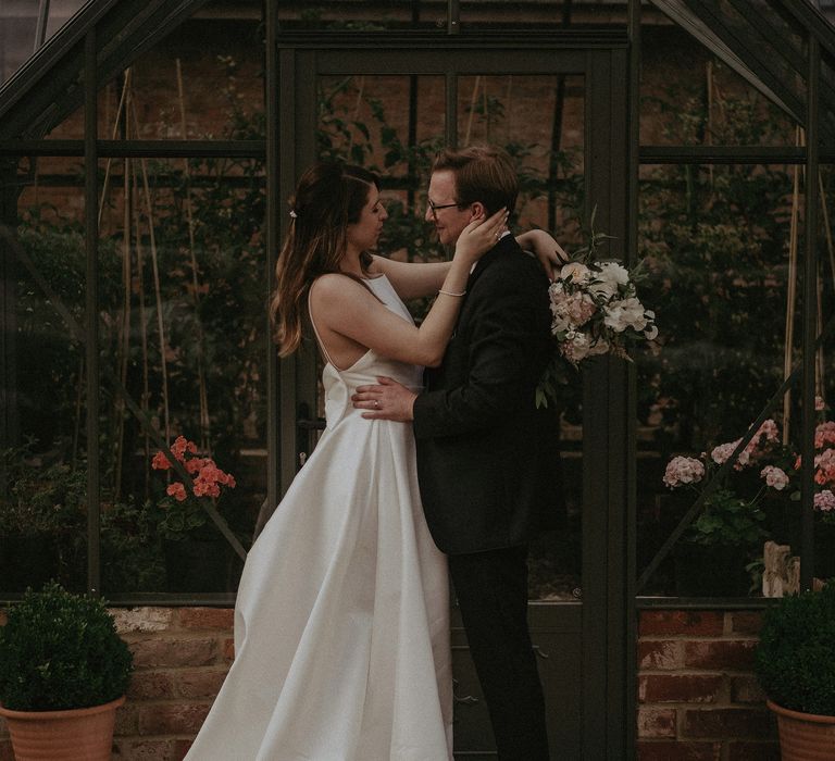 Bride & groom embrace outside greenhouse on their wedding day at Elmore Court