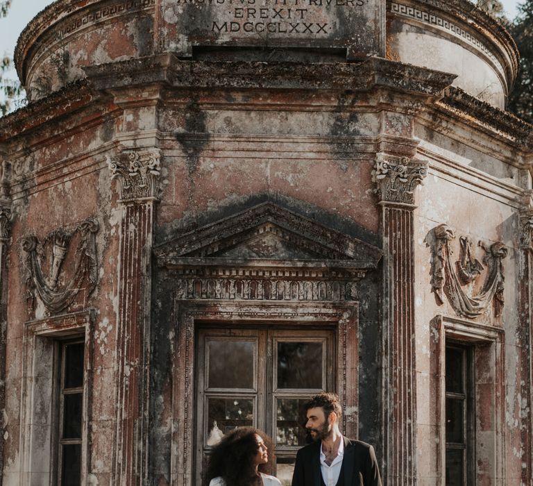 Bride and groom standing by an out building in The Larmer Tree gardens with the groom in a horseshoe waistcoat