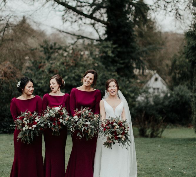 Bridal party portrait with burgundy bridesmaid dresses with long sleeves and bride in a fitted wedding dress with straps and cathedral length veil